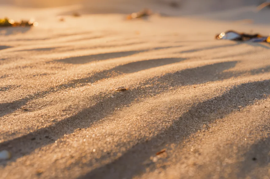 Warmes goldenes Licht spielt über sanfte Wellen aus feinem Sand